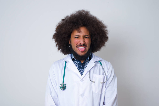 Lichaamstaal. Verafschuwde gestresste dokter in medisch uniform poserend tegen een grijze muur, fronsend gezicht, demonstreerend afkeer van iets. - Foto, afbeelding