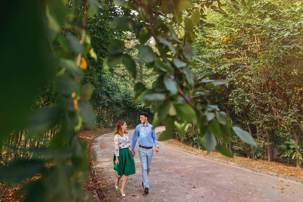 ενός νεαρού ζευγαριού που περπατούσε σε ένα μονοπάτι μέσα από ένα πάρκο πρασίνου. Ένας άντρας και μια γυναίκα περπατούν στην ύπαιθρο. - Φωτογραφία, εικόνα