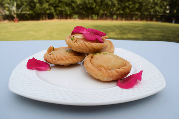 Ινδικό παραδοσιακό γλυκό γνωστό ως Chandrakala, στρογγυλό βαθύ τηγανητό γλυκό από την Ινδία ή το Πακιστάν, φαγωμένο και μαγειρεμένο κατά τη διάρκεια των εορτών. Όπως το Ντιβάλι, το Χόλι, το Ραμαζάν διακοσμημένο με ροδοπέταλα.. - Φωτογραφία, εικόνα