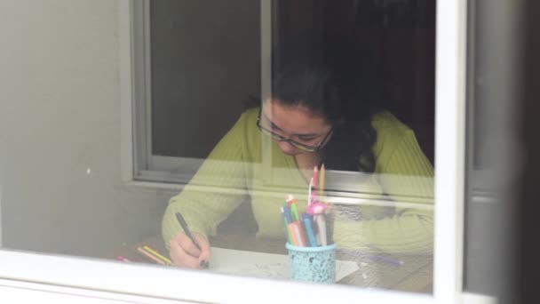 Κορίτσι που φοράει πράσινο πουλόβερ χρωματίζοντας ένα σχέδιο λουλουδιών σε ένα καφέ γραφείο με μερικά διαφορετικά πεκάκια  - Πλάνα, βίντεο