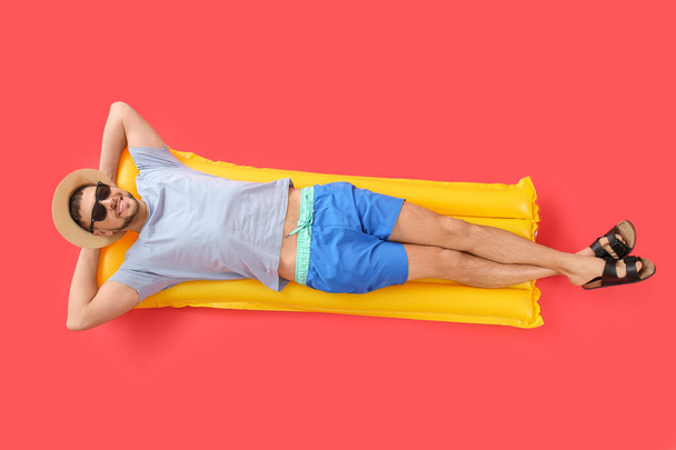 Knappe man liggend op opblaasbare matras tegen kleur achtergrond - Foto, afbeelding