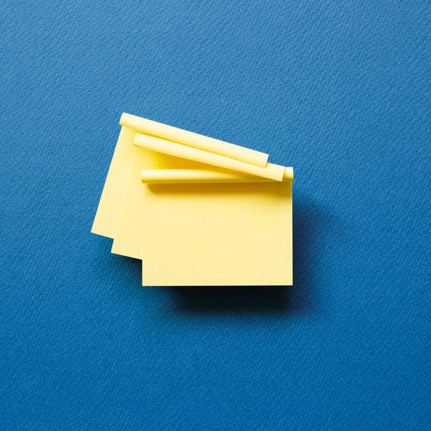 Almohadilla amarilla nota adhesiva sobre fondo azul. vista superior, espacio de copia - Foto, Imagen
