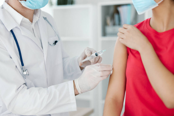 ένας γιατρός με λευκή επικάλυψη κάνει μια ένεση στους ασθενείς με εμβολιασμό βραχίονα - Φωτογραφία, εικόνα