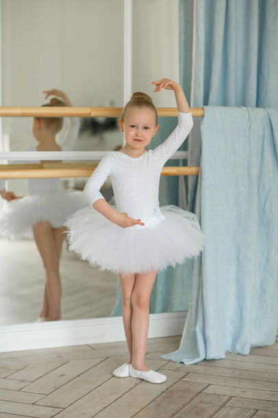 Little sweet girl a blond ballet dancer in a white tutu and kitschka stands in a pose. The concept of children and sports - Fotó, kép