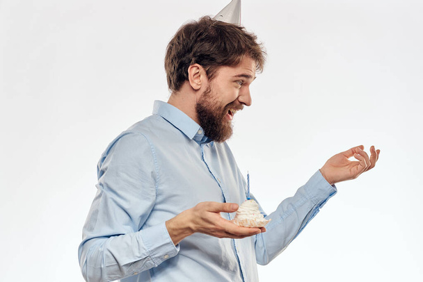 un hombre con barba sostiene un pastel en su mano sobre un fondo claro cumpleaños - Foto, Imagen