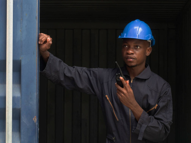 Διευθυντής μηχανικός Φόρμαν αφρικανικό μπλε καπέλο μαύρη σκιά ασφάλειας συζήτηση τηλέφωνο έκθεση εργασίας έκθεση αποθήκευσης εμπορευματοκιβώτιο εισαγωγής εξαγωγή επιχείρηση ιστοσελίδα πελάτη logistic παγκόσμια διεθνή   - Φωτογραφία, εικόνα