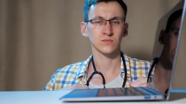 Młody człowiek diagnozuje laptopa za pomocą fonendoskopu - Materiał filmowy, wideo
