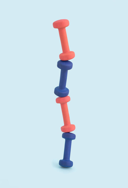 Poids haltères d'exercice rose et bleu empilés dans une tour défiant la gravité pour un concept de fitness unique et minimal sur fond clair. - Photo, image
