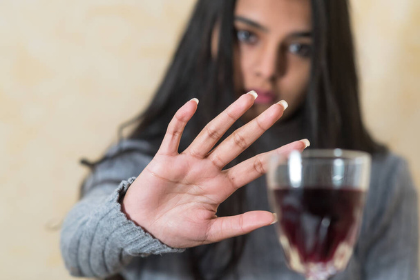 Να κόψω το αλκοόλ. Μια νεαρή γυναίκα στο τραπέζι αρνείται με το χέρι της ένα ποτήρι κόκκινο κρασί. Επιλεκτική εστίαση - Φωτογραφία, εικόνα