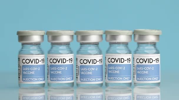 青い背景にテーブルの上に置かれたCOVID 19からワクチンとガラス瓶のコレクションと認識できない医師の閉鎖 - 映像、動画