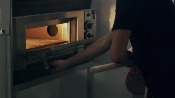 Chef anónimo recortado con pala metálica que toma pizza cruda italiana tradicional preparada para hornear de mesa de mármol en un horno para hornear en la cocina del restaurante - Imágenes, Vídeo