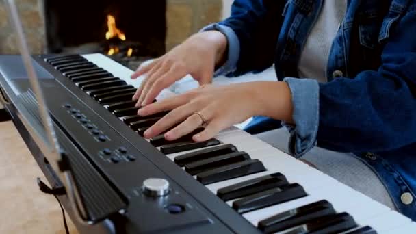 Cosecha femenina en ropa casual sentado en el sofá tocando el piano eléctrico mientras pasa tiempo en casa - Imágenes, Vídeo