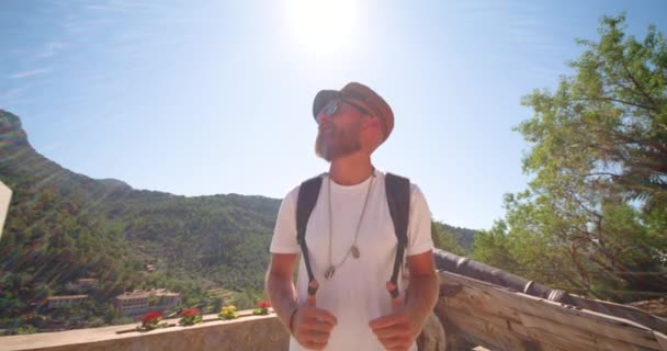 Снизу бородатый турист в стильной одежде, идущий по старинной пушке против гор во время летних путешествий - Кадры, видео
