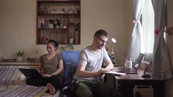 Ocupada pareja de empresarios en ropa casual sentado en el dormitorio y trabajando en línea mientras navega en el ordenador - Metraje, vídeo