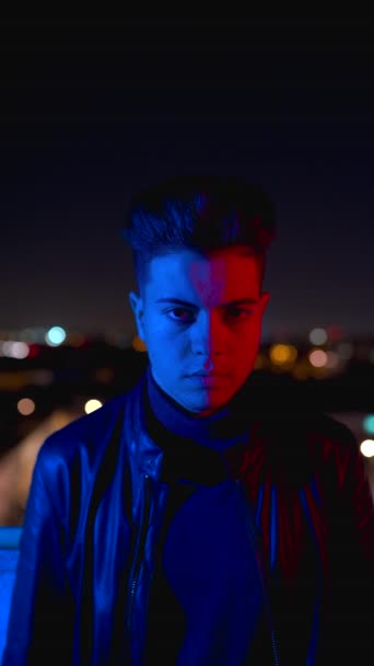 Zeitgenössischer junger Mann verdeckt Gesicht mit der Hand, während er nachts unter grellem roten und blauen Licht auf verschwommenem Hintergrund der Stadtstraße steht - Filmmaterial, Video