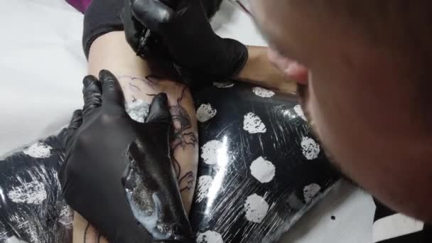 Cultivo tatuaje maestro haciendo contorno en la pierna del cliente - Metraje, vídeo