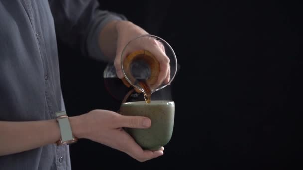 Crop anonyymi naaras kaatamalla tuoretta kuumaa keitettyä kahvia lasi syöttäjä keraaminen kuppi hidastettuna mustaa taustaa vasten - Materiaali, video