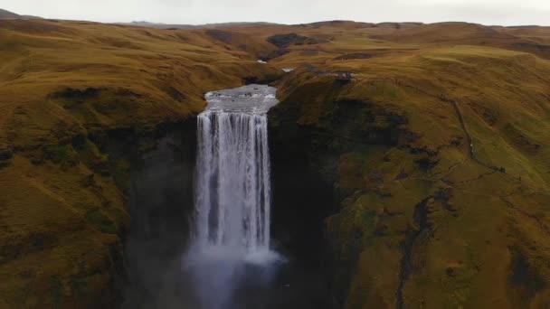 Zoom out vista aerea di ampio flusso di Skogafoss cascata cadere da scogliera verde in natura in Islanda - Filmati, video