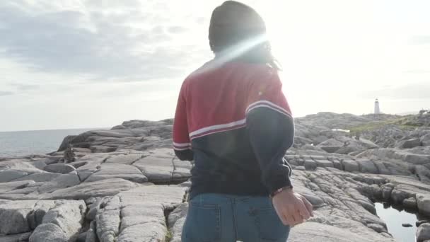 Повернення до анонімної жінки - туристки, що біжить по нерівному кам "яному узбережжі проти сірого хмарного неба біля моря в Пеггіс - Коув (Канада). - Кадри, відео