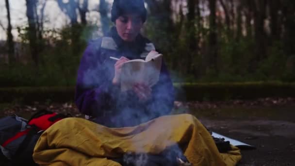 Fiatal női hátizsákos jegyzetel a tábortűznél - Felvétel, videó