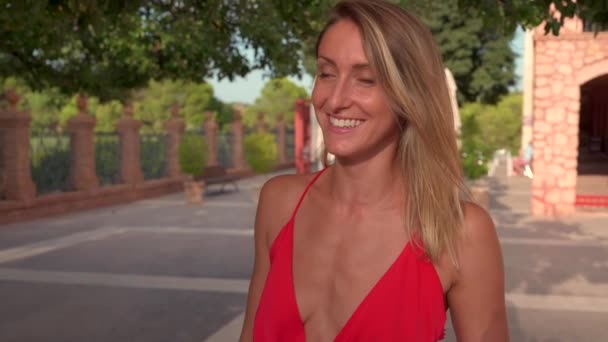 Plan de suivi de la femme ravie en tenue d'été marchant dans un parc verdoyant et profitant des vacances d'été tout en regardant la caméra - Séquence, vidéo
