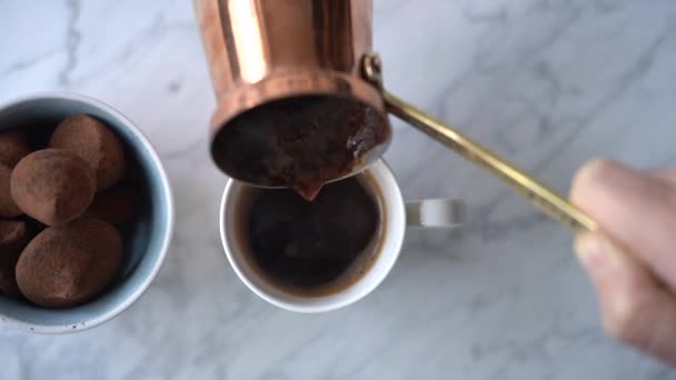Von oben Ernte anonyme Frau gießt heißen gebrühten Kaffee aus der türkischen Kanne in Tasse auf dem Tisch neben Schüssel mit leckeren Süßigkeiten in der gemütlichen Küche zu Hause platziert - Filmmaterial, Video