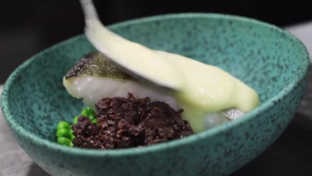 Sluitingen van onherkenbare chef-kok voegen roomsaus toe aan stuk kabeljauwvis in kom op tafel in café - Video