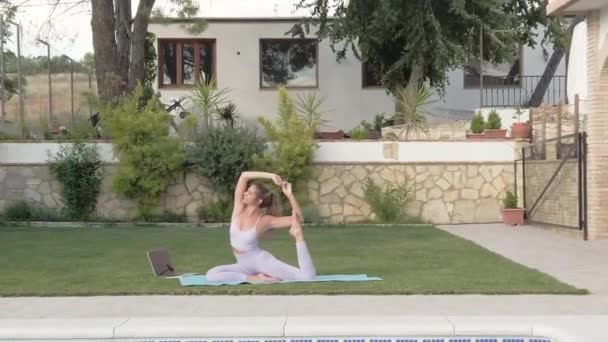 Side view of tranquil female in active wear sitting on mat in Eka Pada Rajakapotasana and practicing yoga in courtyard - Footage, Video