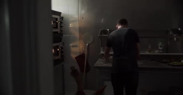 vista trasera de un hombre anónimo irreconocible que usa un rodillo para estirar la masa fresca en la mesa mientras prepara pizza en la cocina - Metraje, vídeo