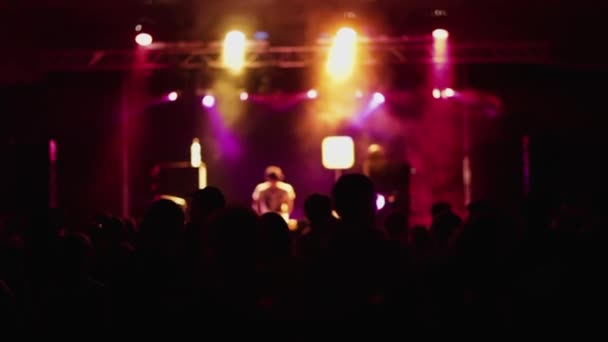 Fiesta nocturna en club moderno con disc jockey tocando música en escenario iluminado con luces de neón y gente bailando - Metraje, vídeo
