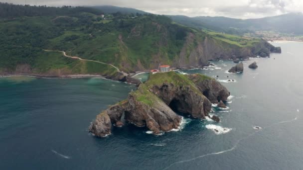 Drone view of paving stone way leading along stone bridge and ridge of rocky hill to lonely house on island Gaztelugatxe surrounded by tranquil sea water under cloudy sky in Basque Country - Metraje, vídeo