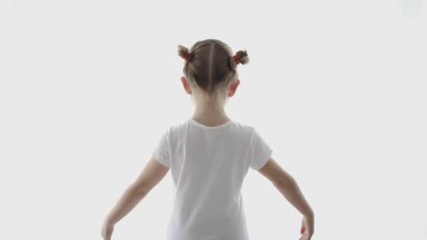 Rückansicht eines nicht wiederzuerkennenden kleinen Kindes in lässigem Outfit, das in einer hellen Wohnung steht und beim Tanzen die Arme ausstreckt - Filmmaterial, Video