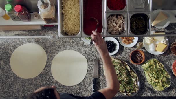 Top näkymä rajattu anonyymi kokki kaatamalla ja levittämällä tomaattikastike taikina kauha kun ruoanlaitto pizza marmoripöydällä eri ainesosia ravintolan keittiössä - Materiaali, video