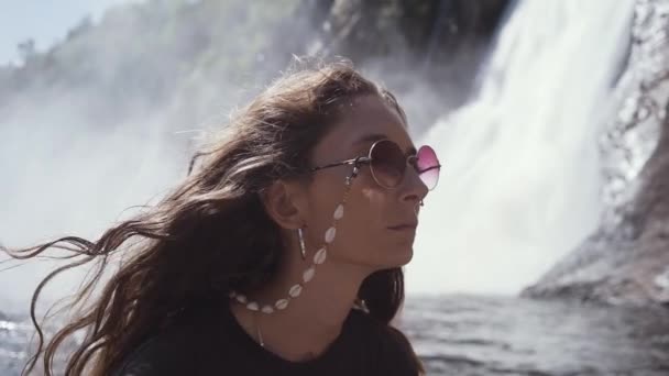 Крупный план замедленной съемки восхитительной молодой женщины-путешественницы с пирсингом и стильными солнечными очками, наслаждающейся свежестью водопадов во время посещения водопада Монморанси в Канаде в солнечный летний день - Кадры, видео