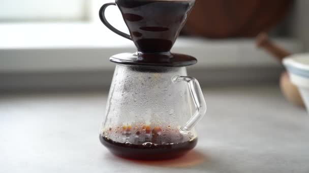 Café caliente elaborado al vapor que gotea del filtro de papel en la olla de cristal colocada en la mesa en la cocina moderna - Metraje, vídeo