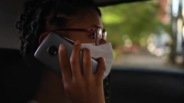 Young afro latina in face mask talking phone in the back seat of a car - Footage, Video