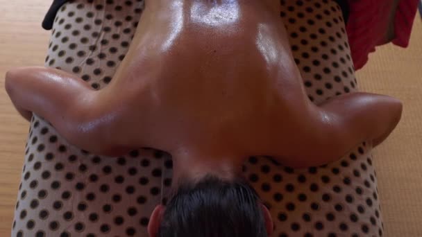 From above crop anonymous master performing ayurvedic massage with aromatic oil on back of relaxed customer in modern salon - Footage, Video