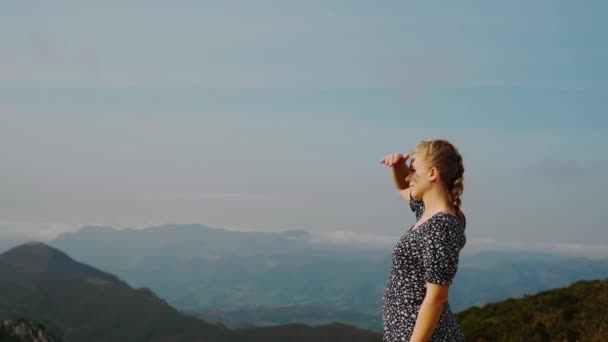 Vista lateral joven hembra positiva con trenza de pie en la colina y disfrutando de pintorescos paisajes de las montañas brumosas - Metraje, vídeo