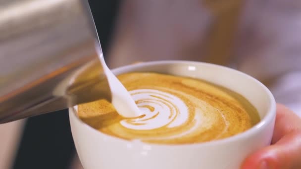Nahaufnahme eines nicht erkennbaren Barista, der heiße Milch aus einem Metallkrug in eine weiße Tasse gießt und daraus aromatischen Cappuccino macht - Filmmaterial, Video