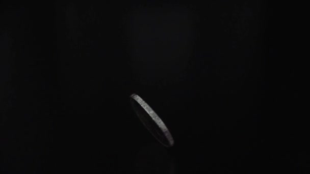 Primo piano moneta metallica che gira su costola al rallentatore in camera oscura su sfondo nero - Filmati, video