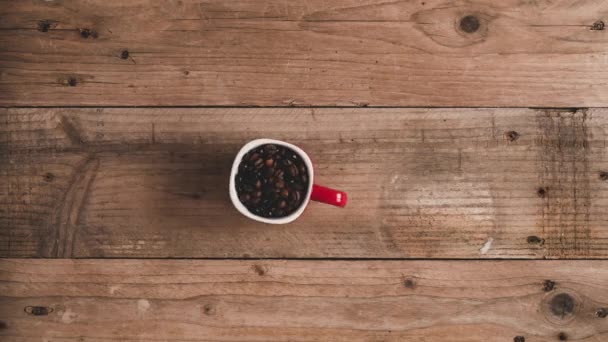 Top view stop motion animace pražených čerstvých kávových zrn v červeném hrnku tvořících nápisy latte na dřevěném stole - Záběry, video