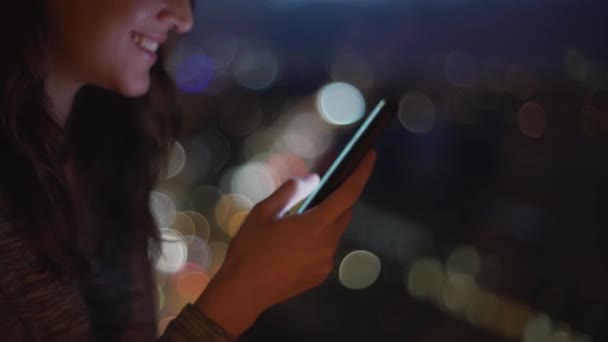 Side view of smiling female using mobile phone and chatting on social media on bokeh background - Footage, Video