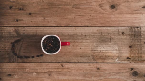 Vista superior stop motion animação de grãos de café frescos torrados em caneca vermelha formando inscrições cappuccino na mesa de madeira - Filmagem, Vídeo
