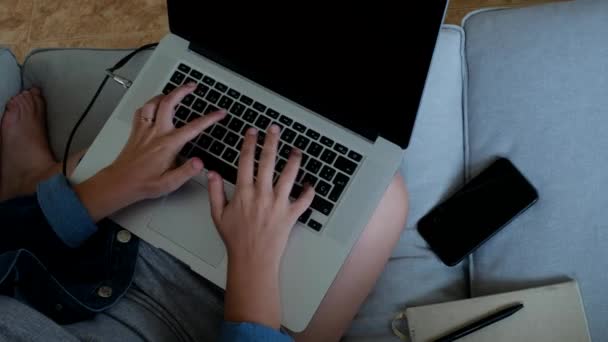 Обрізати молоду жінку, сидячи на дивані і використовуючи ноутбук під час роботи над віддаленим проектом вдома
 - Кадри, відео
