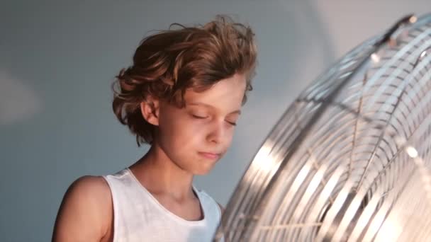 Jongen houdt een lopende ventilator in zijn handen terwijl hij schreeuwt in een kamer - Video