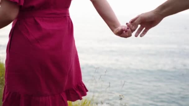 Vystřižené nepoznatelný romantický pár drží za ruce, zatímco stojí na okraji drsné skalnaté útesu proti moři při západu slunce - Záběry, video