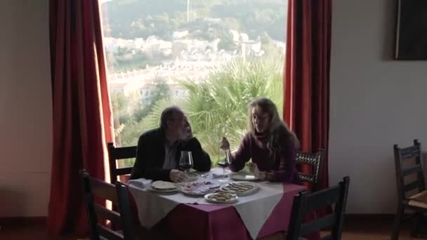 У віці пара розмовляє, вечеряючи разом за столом з посудом і вином в ресторані з мальовничим видом на природу з вікна
 - Кадри, відео