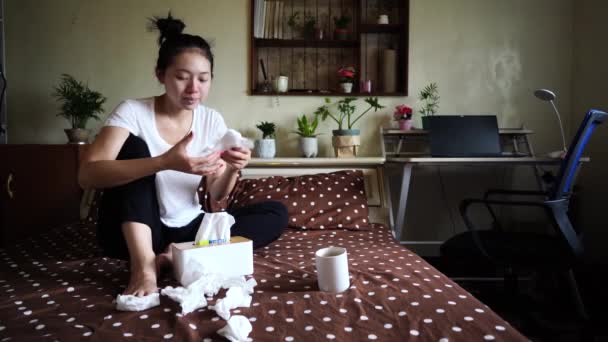 Frowned ethnic female in domestic clothes sitting on bed with running nose while having cold - Imágenes, Vídeo