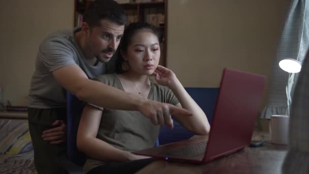 Pareja multiétnica que tiene problemas con la computadora mientras trabajan juntos en el proyecto en línea - Metraje, vídeo