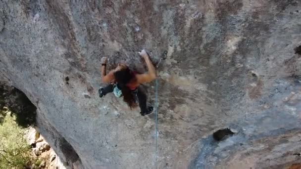 Fentről drón kilátás aktív női alpinista sportruházat kötél és biztonsági felszerelés emelkedő sziklás lejtőjén magas hegy a napsütéses napon - Felvétel, videó